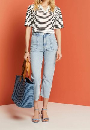 Haut à manches courtes rayé, jean taille haute bleu clair, sandales à lanières bleues et sac fourre-tout tissé bleu avec des accents bruns.