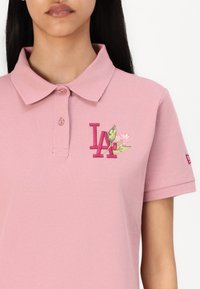 Rosa polo shirt med krage. Utrustad med broderad "LA" logo och blommönster med gröna blad. Texturerad tyg, korta ärmar.