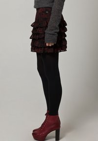 Svart volangkort kjol med ett lagerdesign, kompletterad med en grå stickad tröja och röda snörade ankelstövlar med tjock klack.