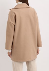 Abrigo de mezcla de lana beige con un amplio cuello, corte holgado y hombros caídos, que presenta bolsillos laterales y una textura suave.