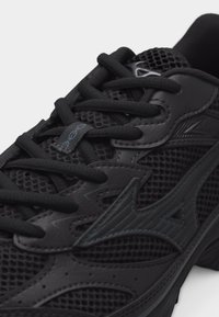 Κοντινή λήψη ενός μαύρου αθλητικού παπουτσιού με διχτυωτό ύφασμα, δερμάτινες επενδύσεις, μαύρα κορδόνια και ένα στυλιζαρισμένο λογότυπο στο πλάι.