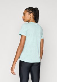 Αθλητική μπλούζα σε ανοιχτό τιρκουάζ με κοντά μανίκια, υφασμάτινη με υφή και λογότυπο στο πίσω μέρος. Φοράται με μαύρο κολάν.