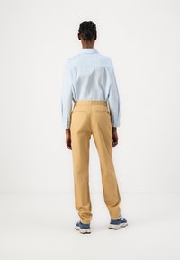 Cămașă albastră deschis, cu mâneci lungi, asortată cu pantaloni bej și adidași albastre. Pantalonii au buzunare la spate.