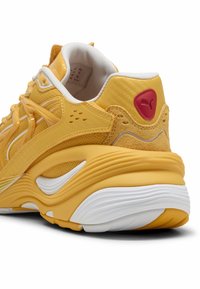 Baskets jaunes avec une tige en maille, des accents en daim texturé, une semelle intermédiaire blanche avec des rainures et un logo rouge au niveau du talon.