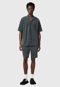 Donkergrijze korte mouwen shirt en bijpassende shorts van zachte stof, met een ontspannen pasvorm en knoopsluiting, gecombineerd met zwarte instappers.