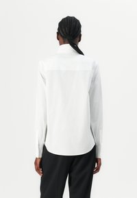Weißes Langarmhemd mit Button-Down-Kragen, glattem Stoff und geradem Saum hinten. Mit Knopfmanschetten.