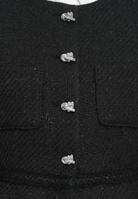 Zwarte tweed jas met een gestructureerde stof, zes zilveren sluitingen, twee voorzakken en een gestructureerde halslijn.