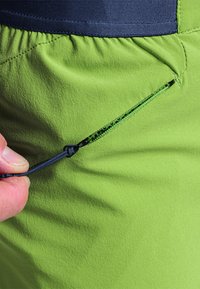 Vihreät ulkoshortsit, joissa on teksturoitu kangas, joustava vyötärö ja vetoketjullinen tasku, jota pidetään sormilla.
