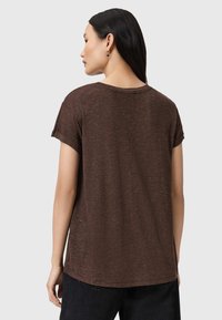 Camicia marrone a maniche corte con vestibilità ampia, scollo rotondo e orli arrotolati. Tessuto leggero con sottili macchie, orlo curvo sul retro.