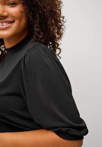 Zwarte, lichte blouse met een hoge halslijn, pof korte mouwen en een gladde textuur, die subtiele draping en een ontspannen pasvorm toont.