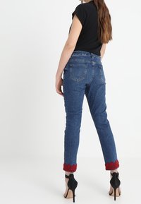 Jeans i denim med en åtsittande passform, med en röd virkad kant vid vristen. Bärs med en svart kortärmad topp och svarta klackar.