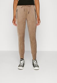 Jogging en suédine marron avec jambes fuselées, taille à cordon de serrage et poches latérales zippées, associés à des baskets montantes noires.