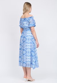 Blauwe jurk met patroon, zonder schouders, met een aansluitend lijfje en een vloeiende midi-rok, met bloemen- en geometrische ontwerpen. Draag het met witte hakken.