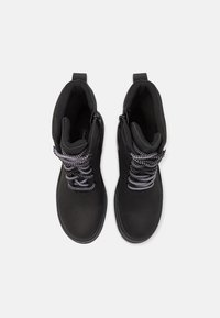 Para czarnych botków za kostkę z czarno-białymi sznurowadłami, bokami na zamek błyskawiczny i pętelkami do ściągania, widziana z góry na białym tle.