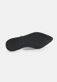 Sole in gomma nera con superficie texturizzata e tacco leggero. La parte superiore è di colore chiaro, realizzata con un materiale liscio e dal design minimalista.