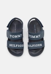 Granatowe sandały z dwoma regulowanymi paskami, na których widnieją białe napisy "TOMMY" i "HILFIGER". Teksturowana wkładka i materiał o wysokiej trwałości.