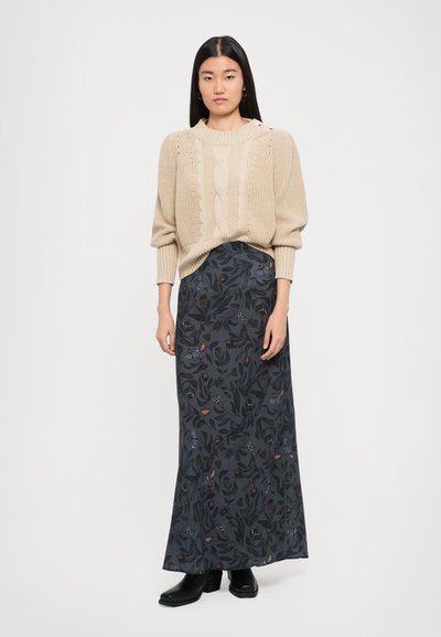 Beige knitted sweater with cable knit design and wide sleeves paired with a dark floral printed maxi skirt. Black chunky heeled ankle boots.