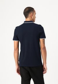 Námořnická polokošile s krátkým rukávem, s bílým lemováním límce a rukávů. Vyrobeno z hladkého materiálu s minimalistickým designem.