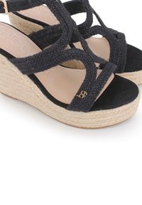 Sandalias de cuña trenzadas negras con plataforma de yute, que presentan un diseño de tiras cruzadas y un detalle en dorado. Textura de ante suave en la plantilla.