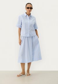 Light blue striped short-sleeve button-up shirt paired with a matching long skirt, featuring a relaxed fit and side pockets, complemented by white flip-flops.