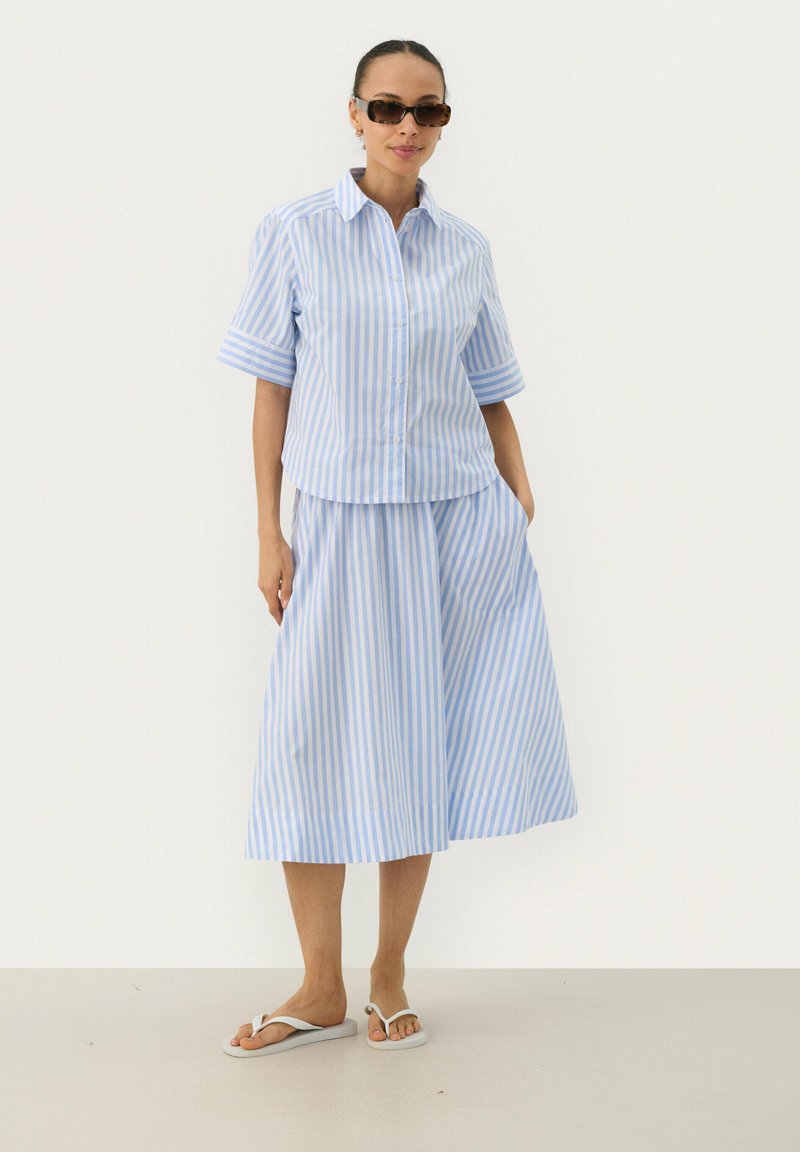 Light blue striped short-sleeve button-up shirt paired with a matching long skirt, featuring a relaxed fit and side pockets, complemented by white flip-flops.