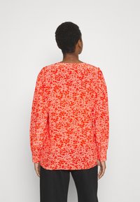 Langärmlige Bluse mit einem lebhaften roten und pinken abstrakten Muster. Mit Rundhalsausschnitt und enganliegenden Manschetten. Leichter Stoff.
