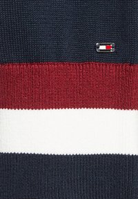 Granatowy sweter dzianinowy z poziomymi paskami w kolorze czerwonym, białym i szarym, z małym logo na lewym boku.