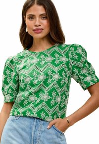 Blusa verde a maniche corte con ricami bianchi floreali e a zigzag dettagliati, scollatura arrotondata e maniche leggermente a sbuffo.
