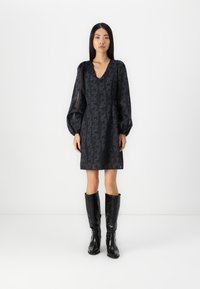 Robe noire à motifs avec un décolleté en V et de longues manches bouffantes, associée à des bottes noires en cuir crocodile jusqu'aux genoux. Texture lisse dans l'ensemble.