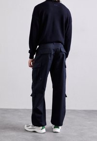 Marineblå cargobukser med flere lommer, afslappet pasform, lavet af stof med en glat tekstur. Kombineret med grå og grønne træningssko.