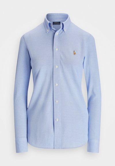Camisa azul-clara de botões com mangas longas, colarinho pontudo e um logo bordado no peito. Feita de um tecido texturizado.
