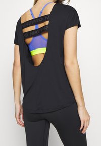 Svart atletisk t-shirt med en stor skärning på baksidan som avslöjar en blå och neongrön sport-bh med svarta remmar märkt "NIKE PRO". Slät textur, korta ärmar.