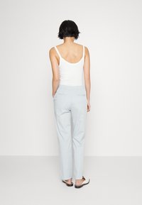 Bílý top bez rukávů s kulatým výstřihem na zádech, v kombinaci s světle modrými volnými kalhotami s jednoduchým designem a elastickým pasem.