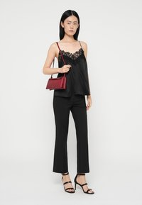 Must musträtik, millel on pitsäär, koos mustade laienevate pükstega. Aksessuaarideks on väike punane käekott ja mustad rihmadega kõrged kontsad.