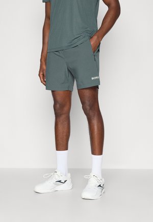 Pánske tmavozelené športové šortky s textúrovanou tkaninou, vybavené bočnou vreckom a bielym logom "BORG". V kombinácii s bielymi ponožkami a topánkami.