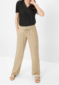Czarna koszulka z dekoltem w serek w połączeniu z beżowymi lnianymi spodniami ze sznurkiem w talii. Spodnie są luźne, z bocznymi kieszeniami i mają fakturowane wykończenie.