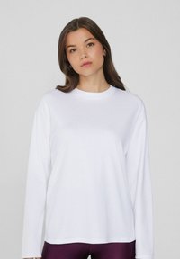 Weißes Langarm-T-Shirt mit Rundhalsausschnitt, aus glattem Stoff gefertigt, mit lockerer Passform und ohne sichtbare Muster oder Akzente.