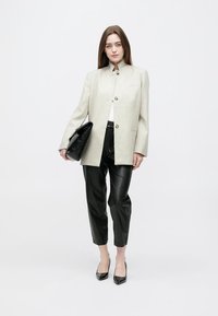 Lysegrå oversized blazer, sorte læderbukser, sorte spidse hæle og clutch. Blazeren har knapper og en ståkrave.