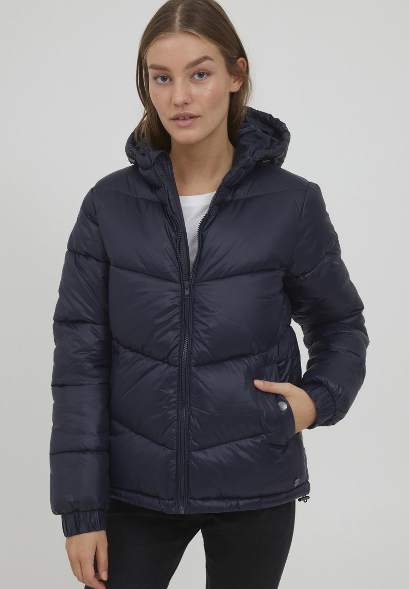 Giacca puffer blu navy con cappuccio, caratterizzata da segmenti trapuntati, zip frontale e polsini elasticizzati. Tessuto sintetico liscio e lucido.