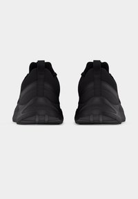 Ζευγάρι μαύρα αθλητικά παπούτσια εμφανίζονται από πίσω πάνω σε απλό ανοιχτό γκρι φόντο.