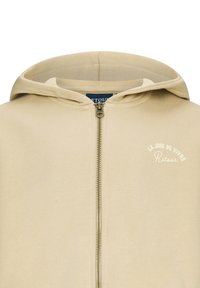 Felpa beige con zip realizzata in un tessuto morbido, caratterizzata da una chiusura frontale con zip, un cappuccio e dettagli in bianco con la scritta "LA JOIE DE VIVRE" sul petto.