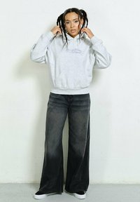 Gray hooded sweatshirt with a front pocket and logo, paired with loose-fitting black denim jeans and white sneakers on a plain background.