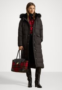 Duga crna puffer jakna s kapuljačom od krzna, koja ima dugmadi s preklapanjem i bočne džepove. Uparena s crvenom kariranom košuljom, crnom suknjom i čizmama do koljena.