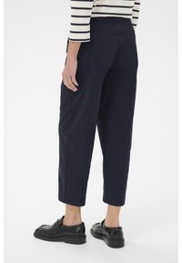 Pantalons courts en marine avec une coupe décontractée, dotés de poches arrière et d'une texture lisse, associés à des chaussures en cuir noires.