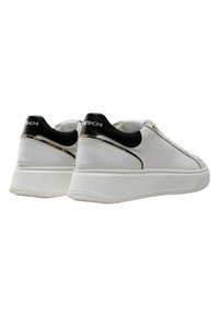 Deportivas blancas con un upper de cuero liso, acentos en el talón de color negro contrastante y una gruesa suela de goma blanca, con un diseño minimalista.