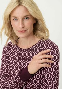 Das Langarmoberteil zeigt ein geometrisches Muster in Pink und dunklem Burgunderrot, mit einem runden Ausschnitt und kontrastierenden Manschettendetails.