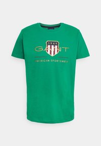Zielona bawełniana koszulka z krótkim rękawem. Posiada logo w kształcie tarczy w kolorze bordowym i kremowym, z napisem "GANT" oraz "AMERICAN SPORTSWEAR" w kolorze złotym.