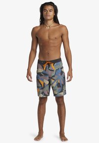 Board shorts in dark tones with a colorful leaf and abstract pattern. Features an adjustable orange waistband and a small logo on the leg.
