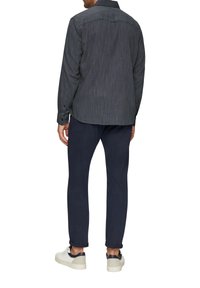 Mannelijk donkergrijs shirt met subtiele verticale strepen, met knoopsluiting aan de mouwen en een gebogen zoom, gecombineerd met marineblauwe broeken en lichte sneakers.
