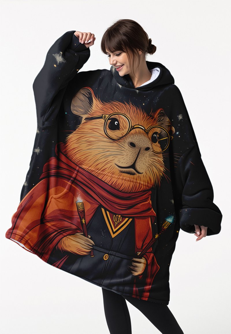 Kvinna som bär en överdimensionerad svart hoodie med en tecknad marsvin i glasögon och röd scarf som håller två lysande magiska stavar.